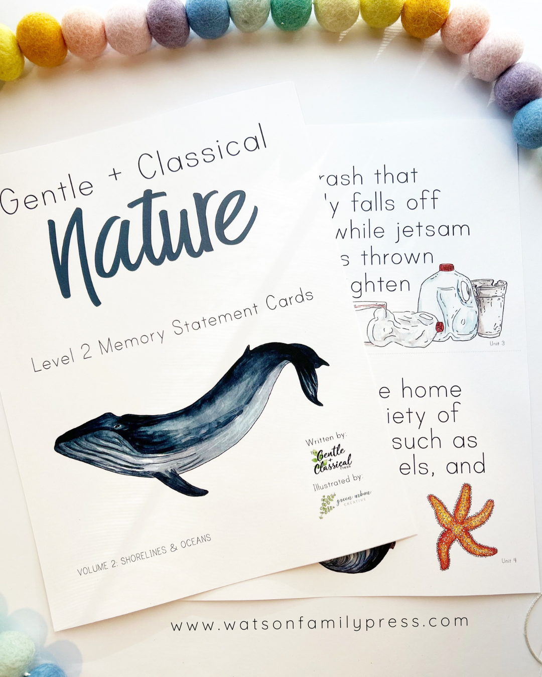 Two printed memory statement cards for children titled 'Gentle + Classical Nature' are shown on a white background with a string of pastel pom-poms around the top edge. The cards feature black text, a blue whale illustration, a small bottle-and-bubble drawing, and a starfish illustration.