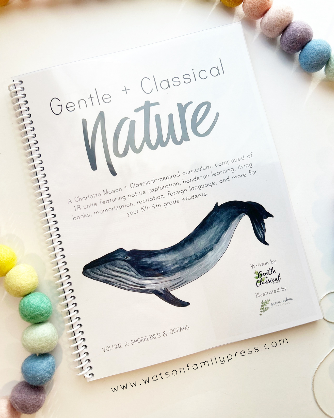 A spiral-bound educational curriculum booklet titled 'Gentle + Classical Nature' with a whale illustration on the cover, photographed on a light surface with colorful felt pom-poms around it.
