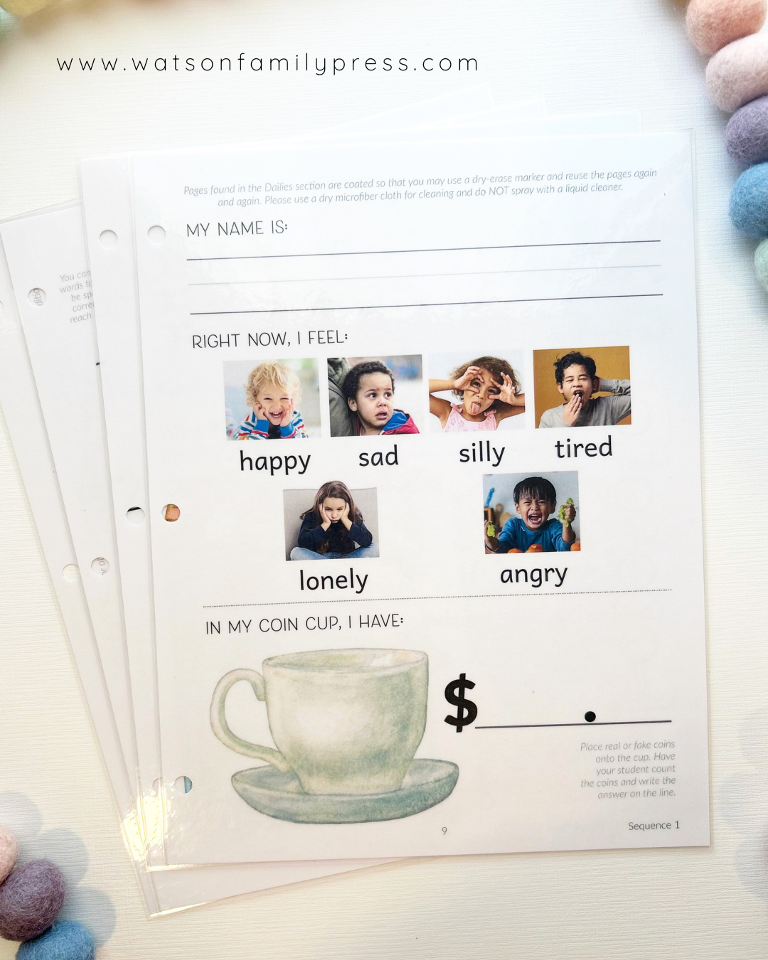 Laminated student sheets with three hole punch styled on a light surface with colorful pom-pom beads around it.