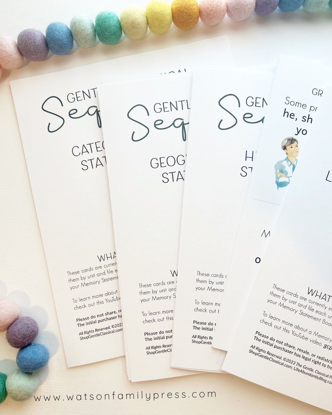 A printed card deck titled 'Gentle + Classical Sequence 1 Memory Statement Cards' for 3-part Montessori cards, featuring partial  illustrations on white cards, photographed on a light surface with colorful pom-poms around the edges.