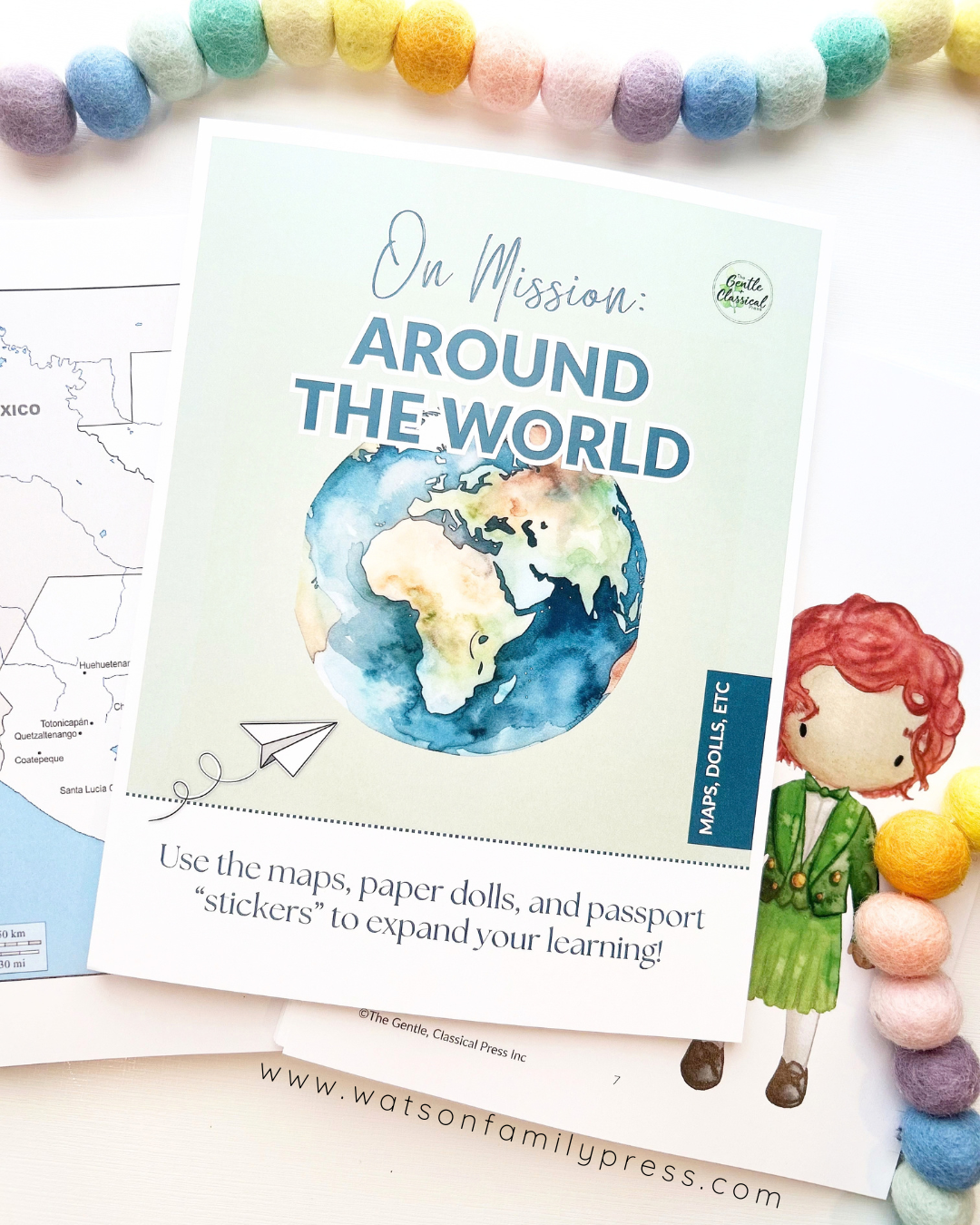 A loose leaf educational curriculum titled 'On Mission Around the World' with an earth illustration on the cover, photographed on a light surface with colorful felt pom-poms around it.