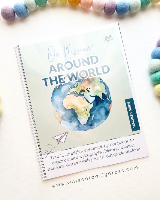 A spiral-bound educational curriculum booklet titled 'On Mission Around the World' with an earth illustration on the cover, photographed on a light surface with colorful felt pom-poms around it.