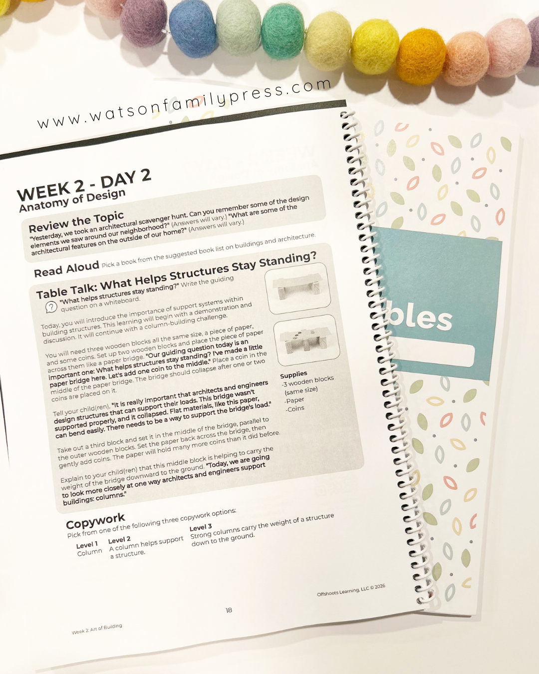 Open educational workbook with pages on a white surface, featuring text and a colorful bead garland at the top.
