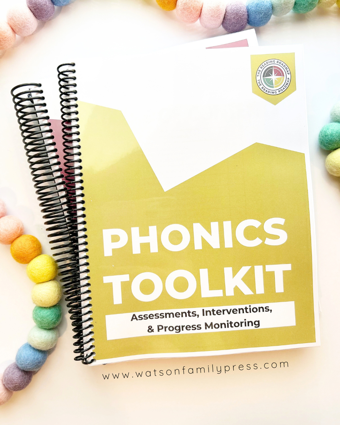 A spiral-bound educational curriculum booklet titled 'Phonics Toolkit' with a yellow front cover, photographed on a light surface with colorful felt pom-poms around it.
