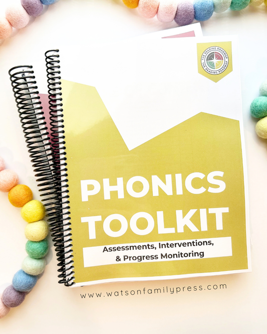 A spiral-bound educational curriculum booklet titled 'Phonics Toolkit' with a yellow front cover, photographed on a light surface with colorful felt pom-poms around it.