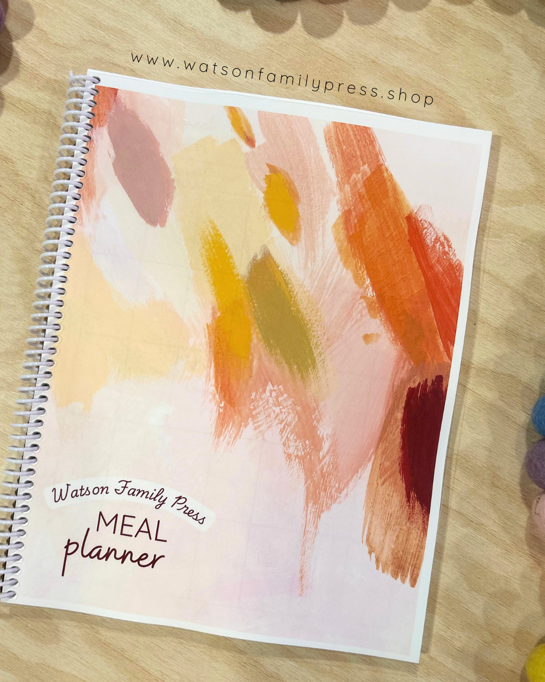 Meal planner with colorful brushstroke abstract design on a wooden surface