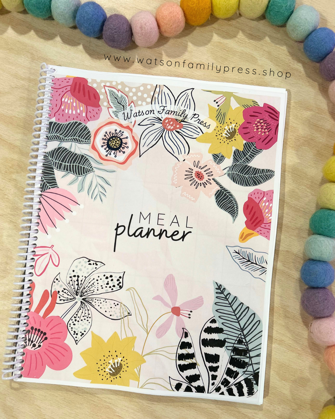 Floral design meal planner on a wooden surface with colorful beads.