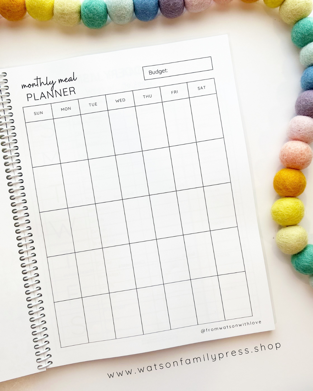 Monthly meal planner, undated monthly calendar page on a white surface with colorful beads around