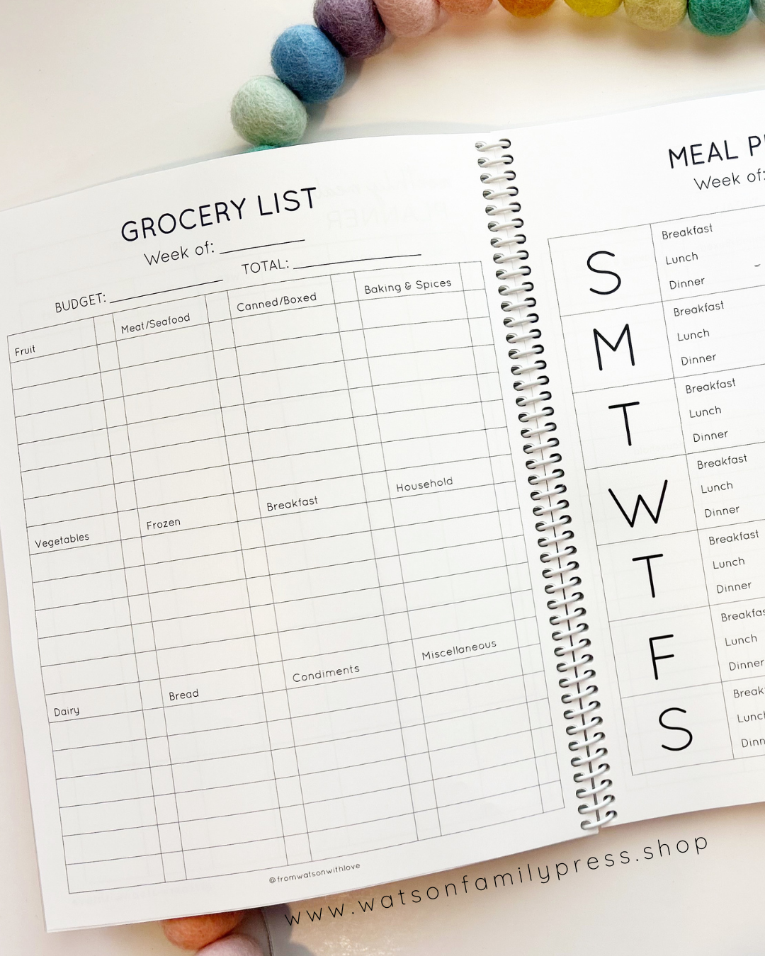 Open spiral-bound planner with grocery list and meal plan pages on a light surface.