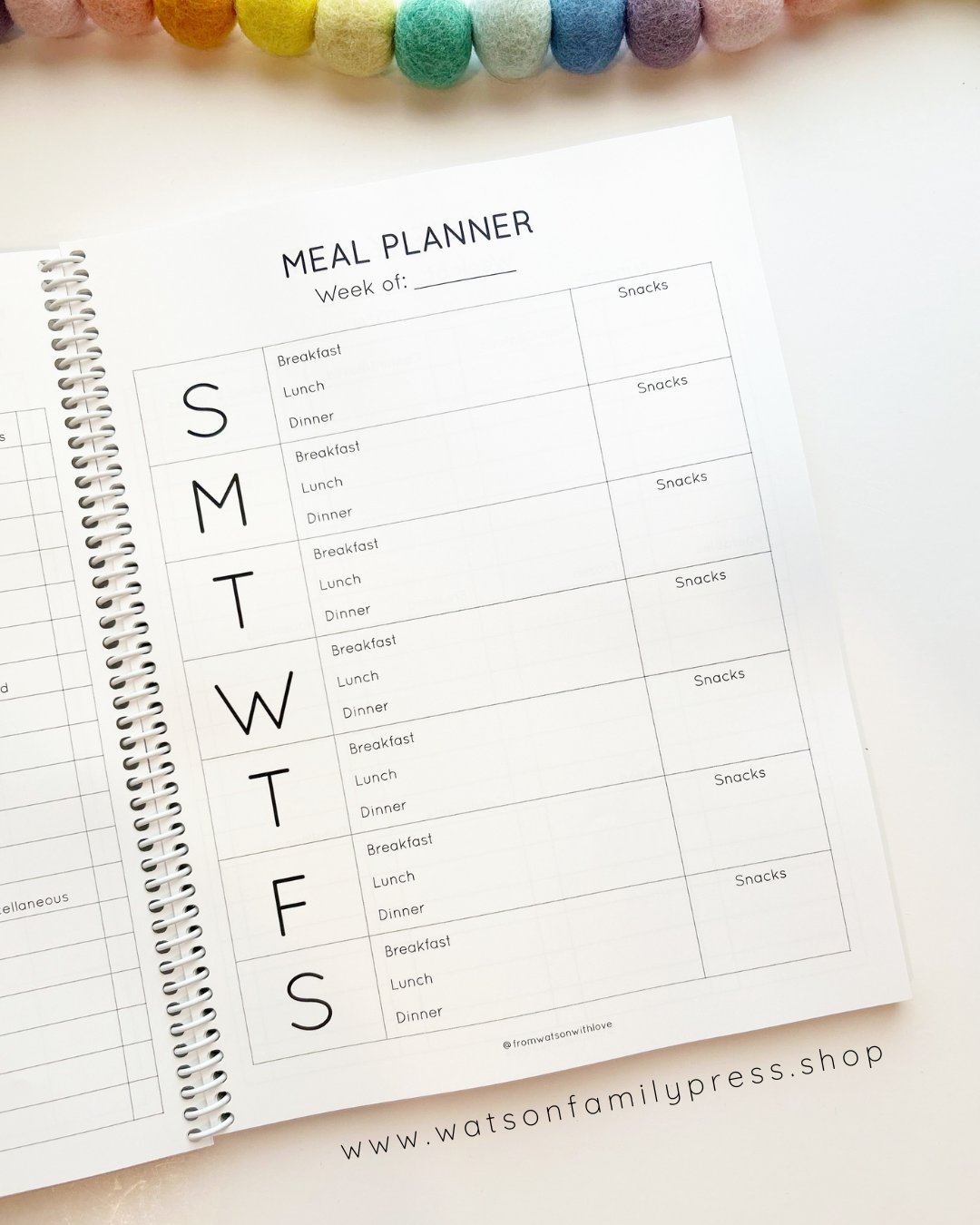 Weekly meal planner sheet on a white surface with a colorful beaded necklace.