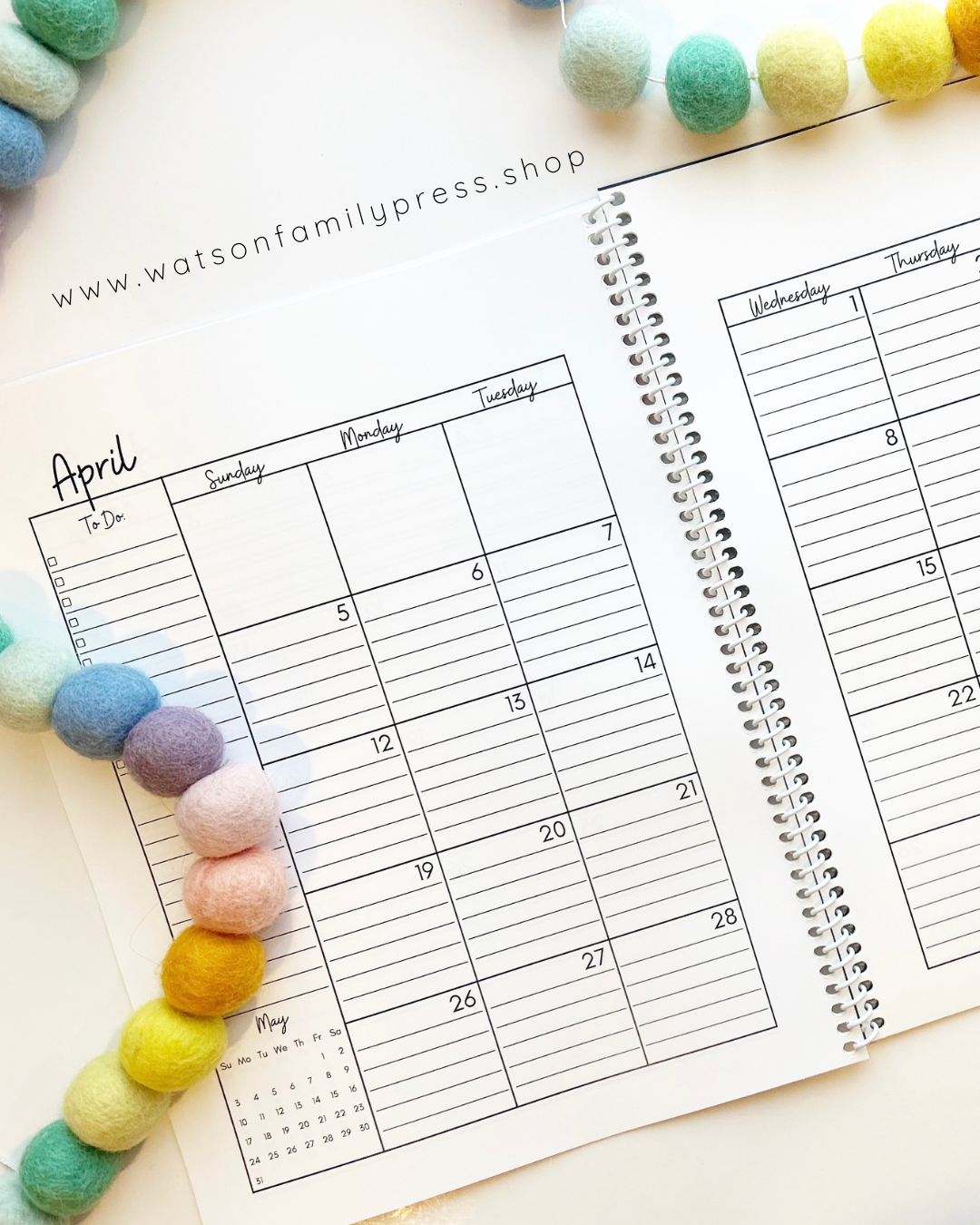 Open spiral bound planner with dated April calendar page and decorative felt balls on a light surface.